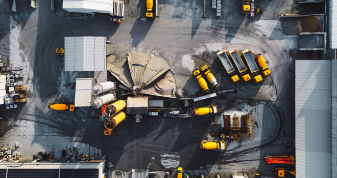Aerial view in industrial area, directly above concrete factory, firm with lots of heavy machinery on the grounds, yellow trucks and other vehicles.