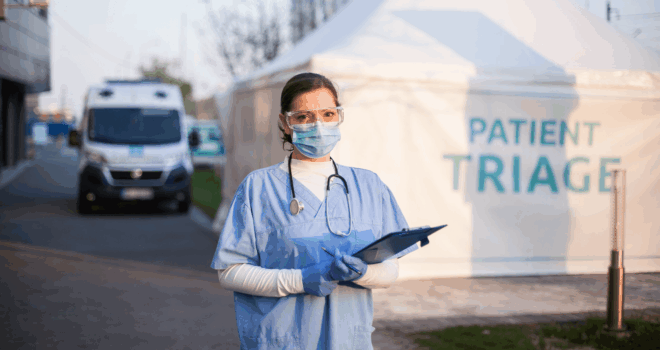 Portrait of serious female key front line worker in blue PPE uniform,standing outside EMS hospital or ICU clinic facility entrance,UK COVID-19 drive through testing site,rt-PCR Coronavirus diagnostic