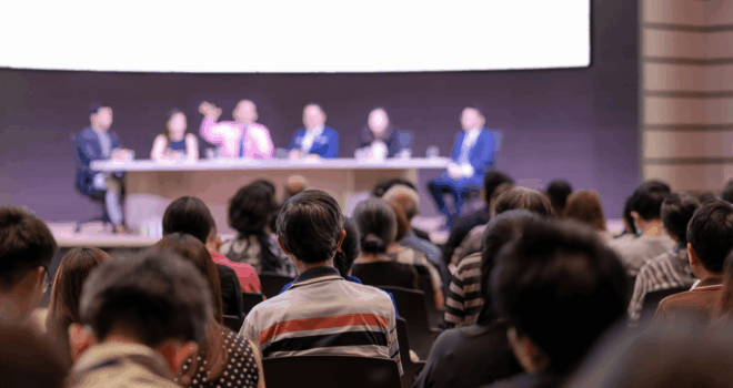 Rear view of Audience in the conference hall or seminar meeting which have Speakers are Brainstorming and talking on the stage, business and education about investment concept