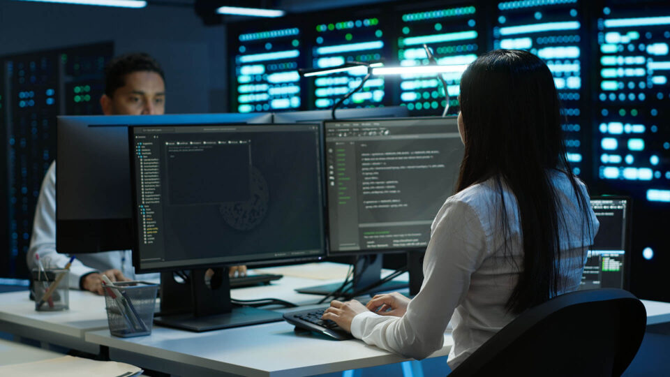 Person in front of computer screens showing code