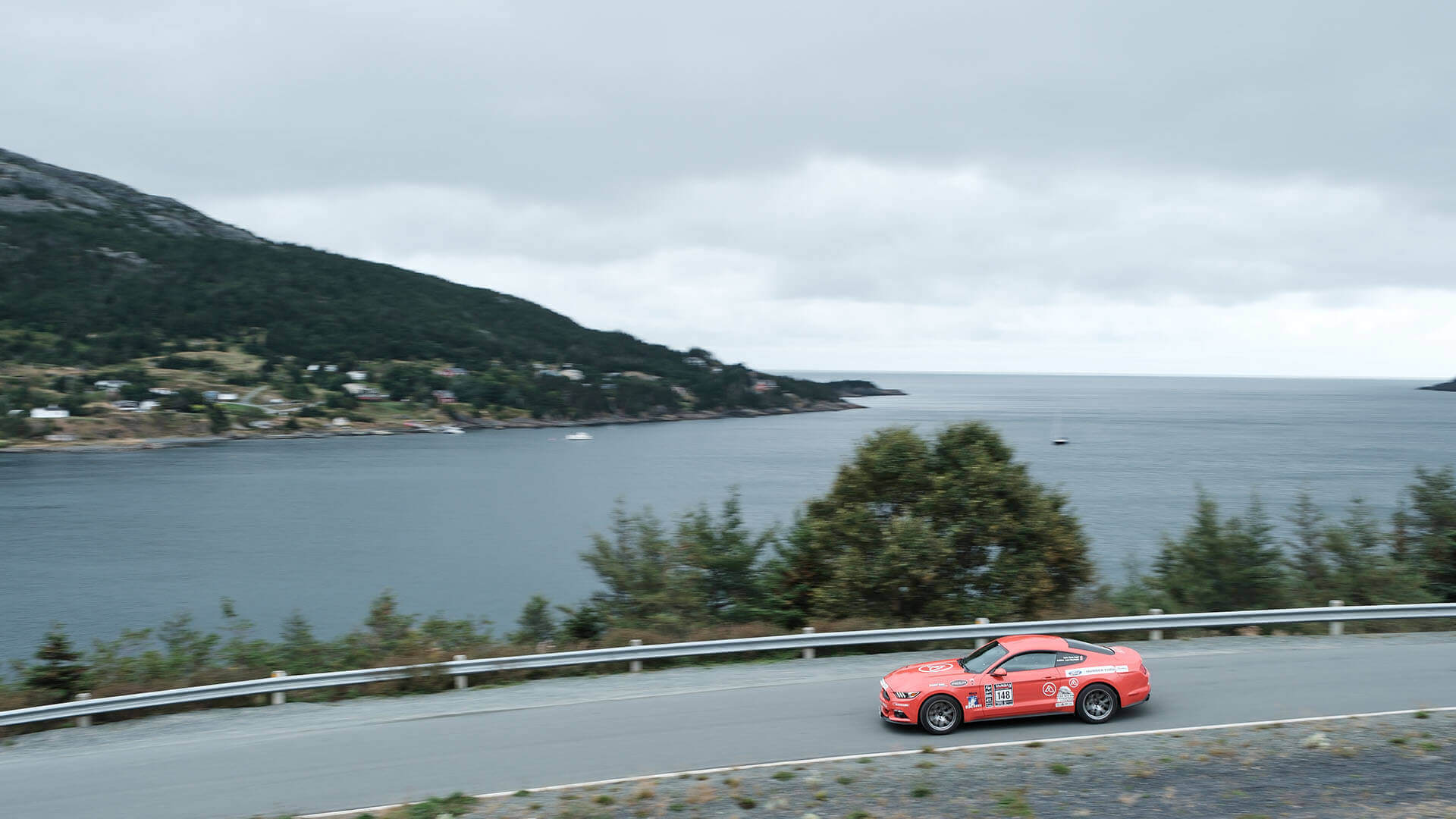 Targa competitor driving on a road with a bay in the background